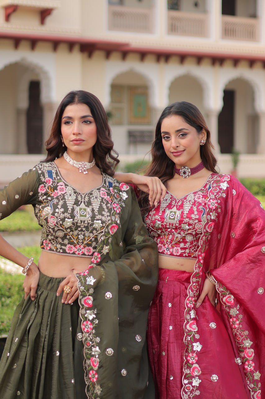 Two women in traditional embroidered outfits standing outdoors with a building in the background.